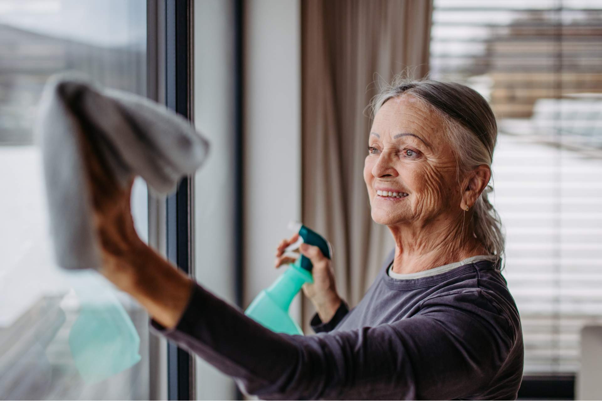 senior woman with cleaning supplies cleaning a window